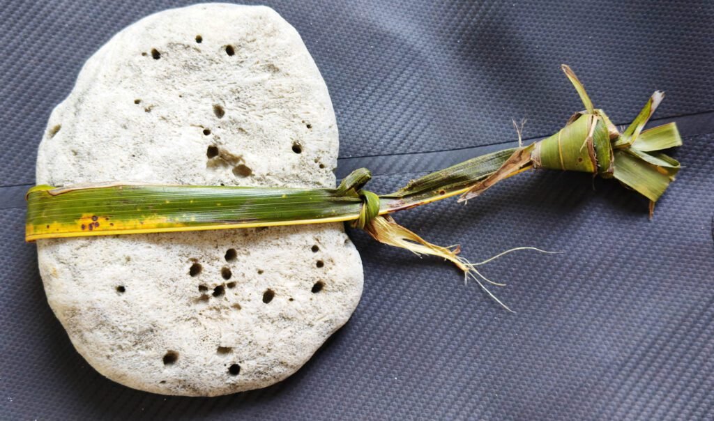 A small smooth stone bound tightly with a dried green palm leaf tied into a knot.