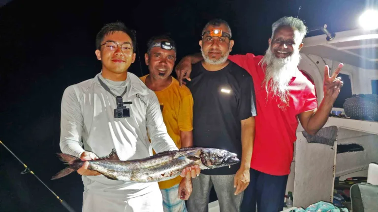 Anglers and local fishermen pausing for a photo while a tourist holds a freshly caught Kattelhi fish on a boat at night in Fuvahmulah.
